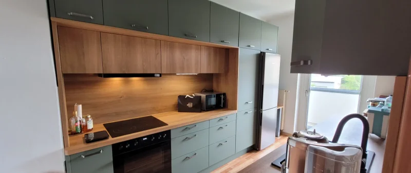 Ansicht einer Küchenzeile in Grün mit Kühlschrank und Holzdekore