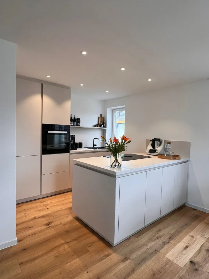 Weiße, moderne Küchenzeile mit Kochinsel - seitliche Ansicht