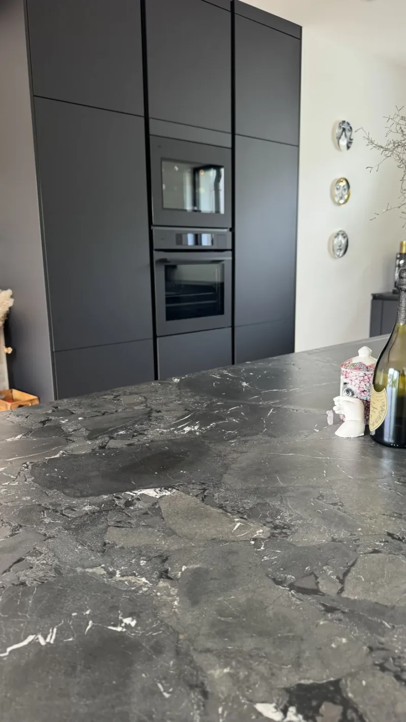 Blick auf die Natursteinarbeitsplatte und im Hintergrund auf den Hochschrank mit integriertem Backofen.