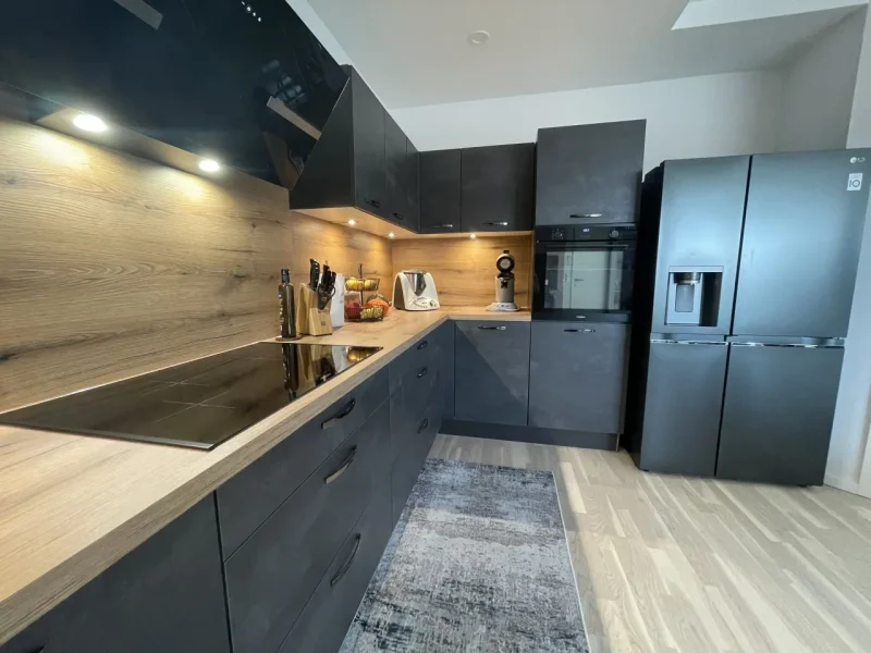 Ansicht des L Flügels mit Hochschrank, eingebautem Backofen und dem danebenstehenden großen Kühlschranks.