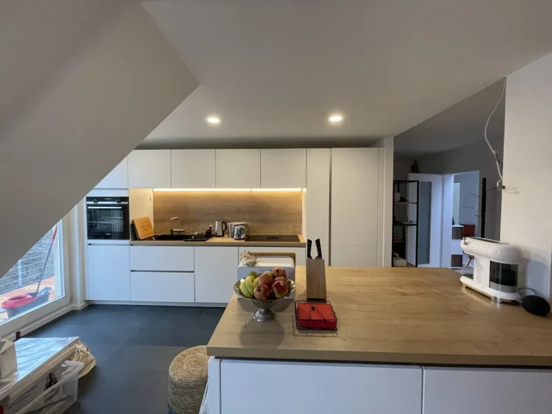 Gesamteindruck der hellen Küche mit Kücheninsel im Vordergrund und der Küchenzeile im Hintergrund.