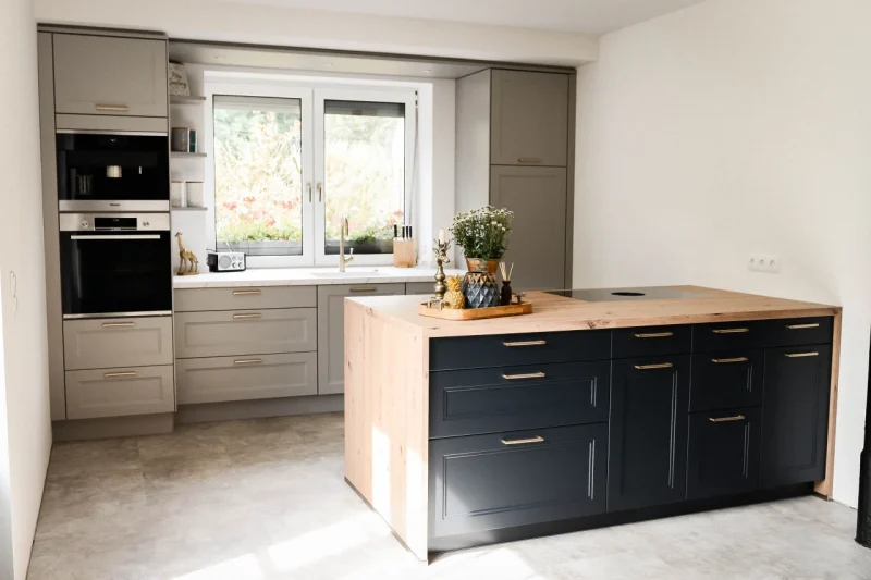 Seitliche Ansicht der Küche, welche den Kontrast zwischen der hellen Küchenzeile und der dunklen Insel hervorhebt.